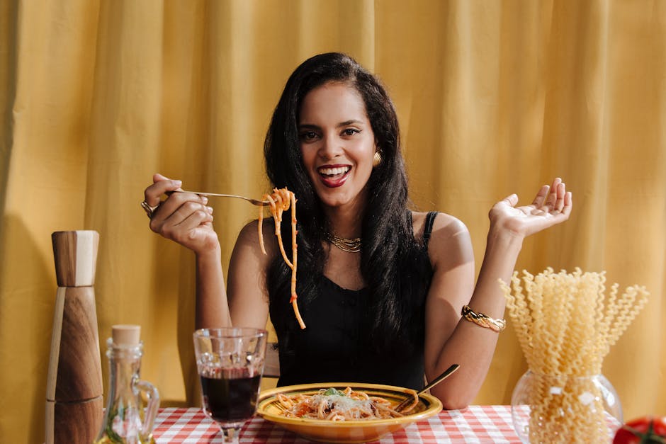 Woman with black hair smiling while enjoying spaghetti in an indoor dining setting