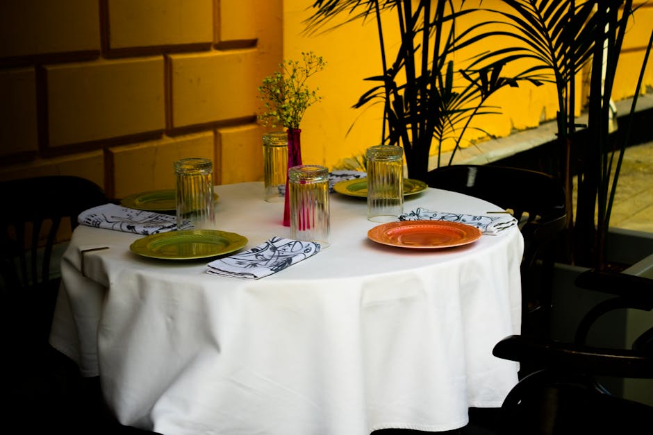 A beautifully set round dining table with colorful plates and glasses, perfect for outdoor dining