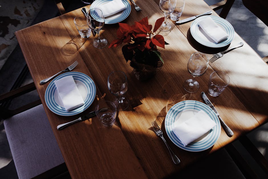 A beautifully set dining table with striped plates and silverware, centered around a red flower arrangement